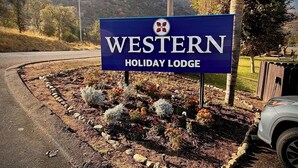 Letrero de Western Holiday Lodge con un jardín ajardinado al frente.