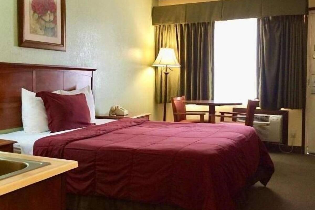 A hotel room with a bed, a desk, a chair, a lamp, and a painting on the wall.