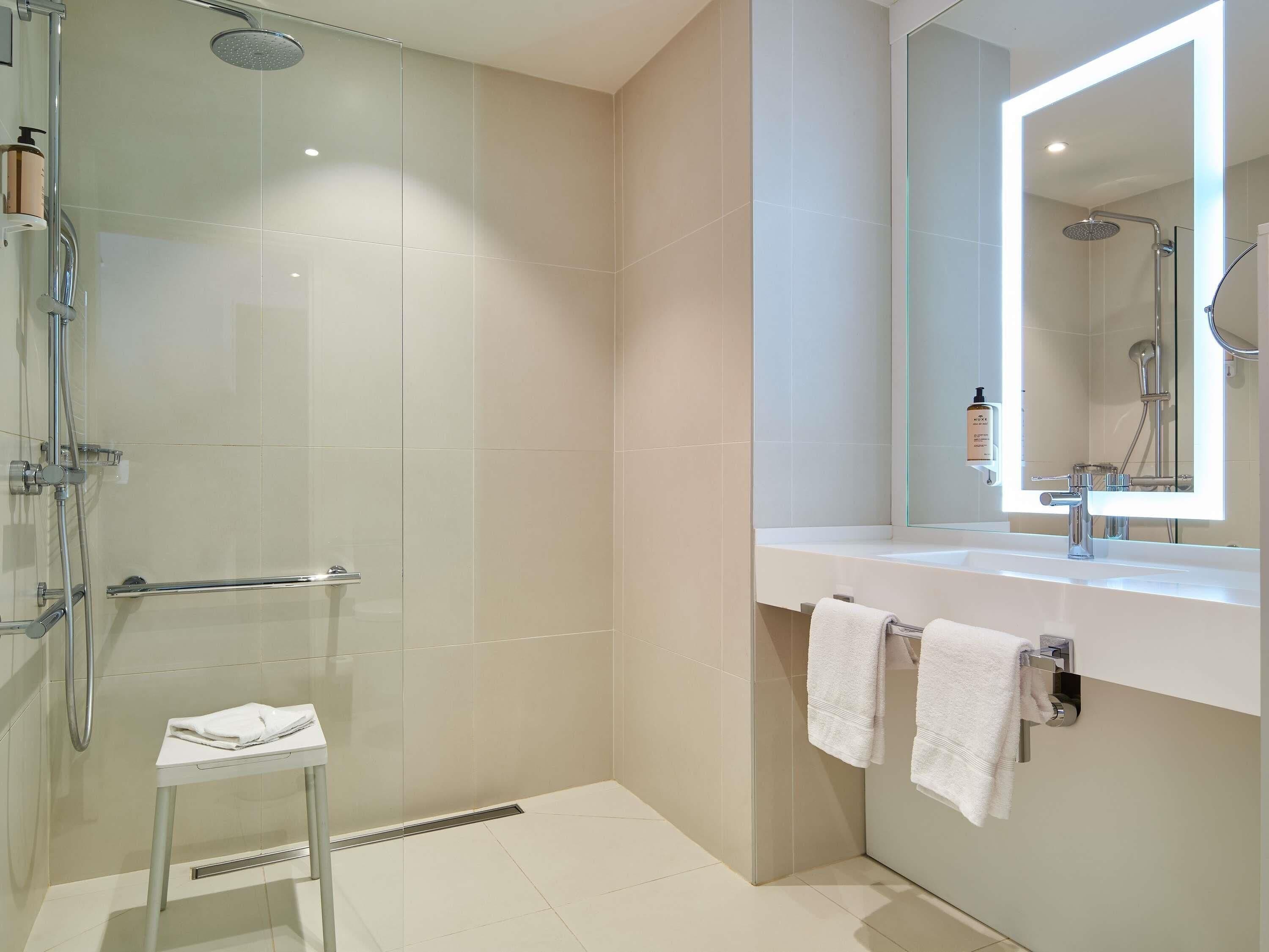 A modern bathroom with a glass shower enclosure, a white vanity with a mirror, and two towels hanging on the wall.