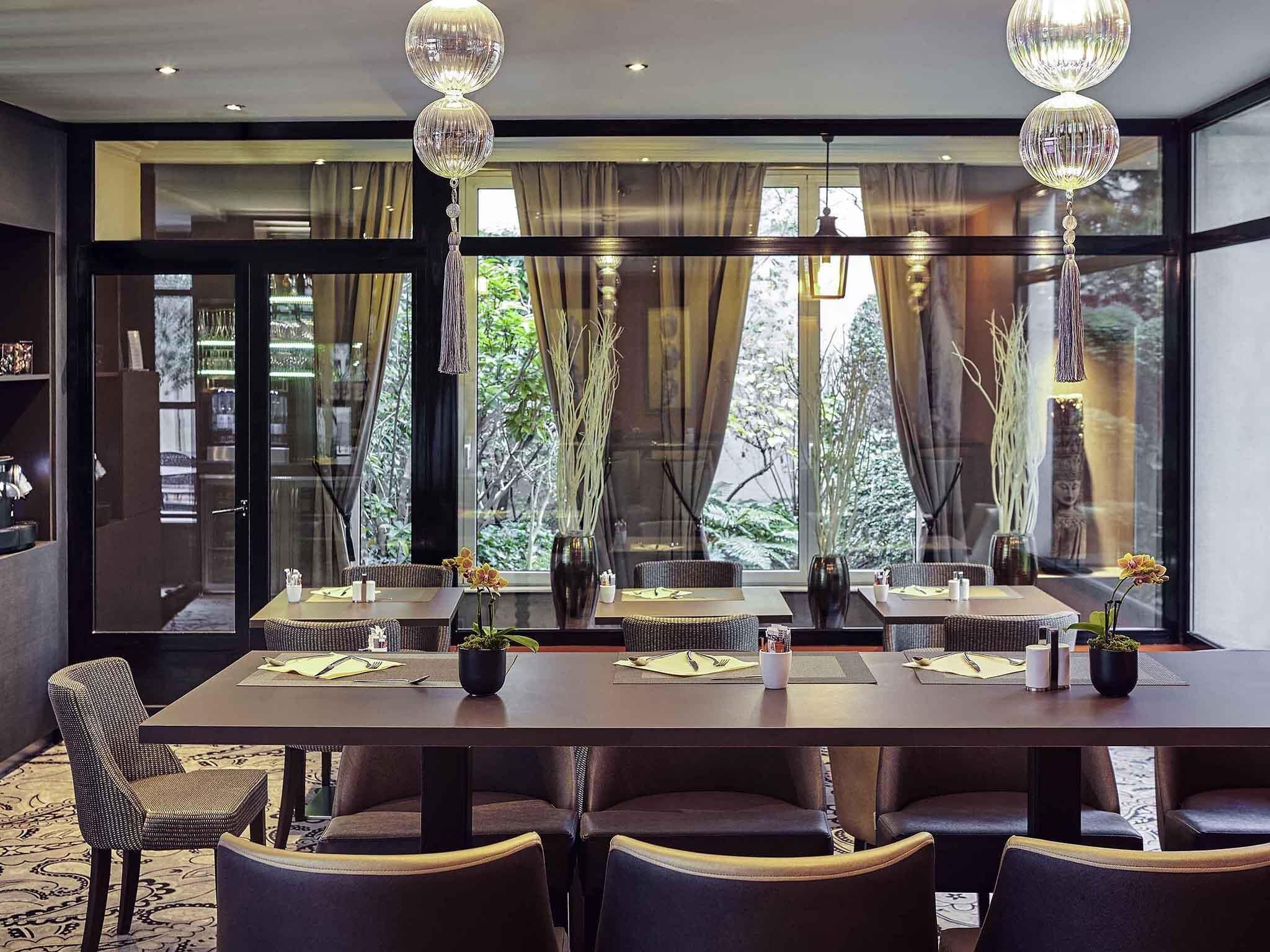A modern dining area with a long table, multiple chairs, and hanging pendant lights.