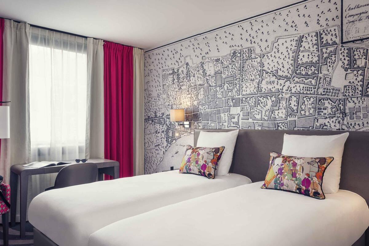 Ein Hotelzimmer mit zwei Betten, einem Schreibtisch, einem Stuhl, einer Lampe und einer großen Karte an der Wand.