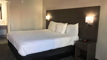 Una habitación de hotel con una cama grande, dos lámparas de noche, una mesita de noche y un reloj digital.