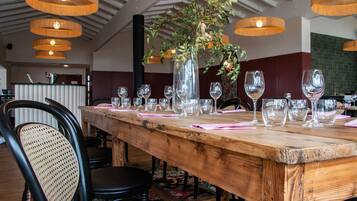 Una mesa de madera para comer con varias copas de vino y un florero con plantas verdes.