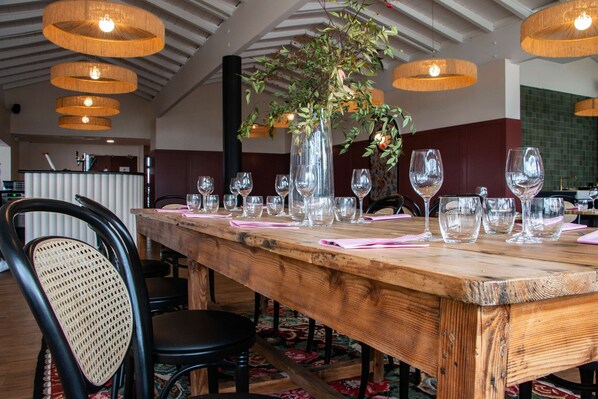 A wooden dining table with multiple wine glasses and a vase with greenery.
