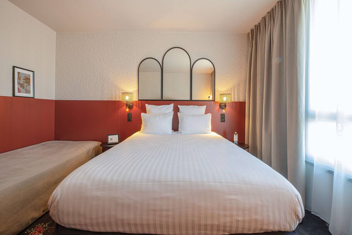 A hotel room with a large bed, a smaller bed, a mirror with three arches, and two bedside lamps.