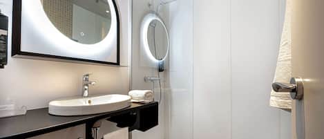 A modern bathroom with a round mirror, a sink, and a shower.