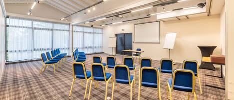 A conference room with rows of blue chairs, a whiteboard, and a projector screen.