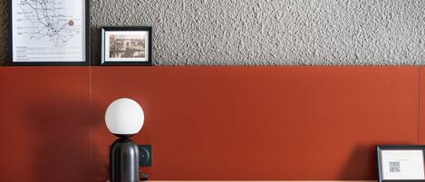 A reception desk with a framed map, a framed photograph, a modern lamp, and a chair.