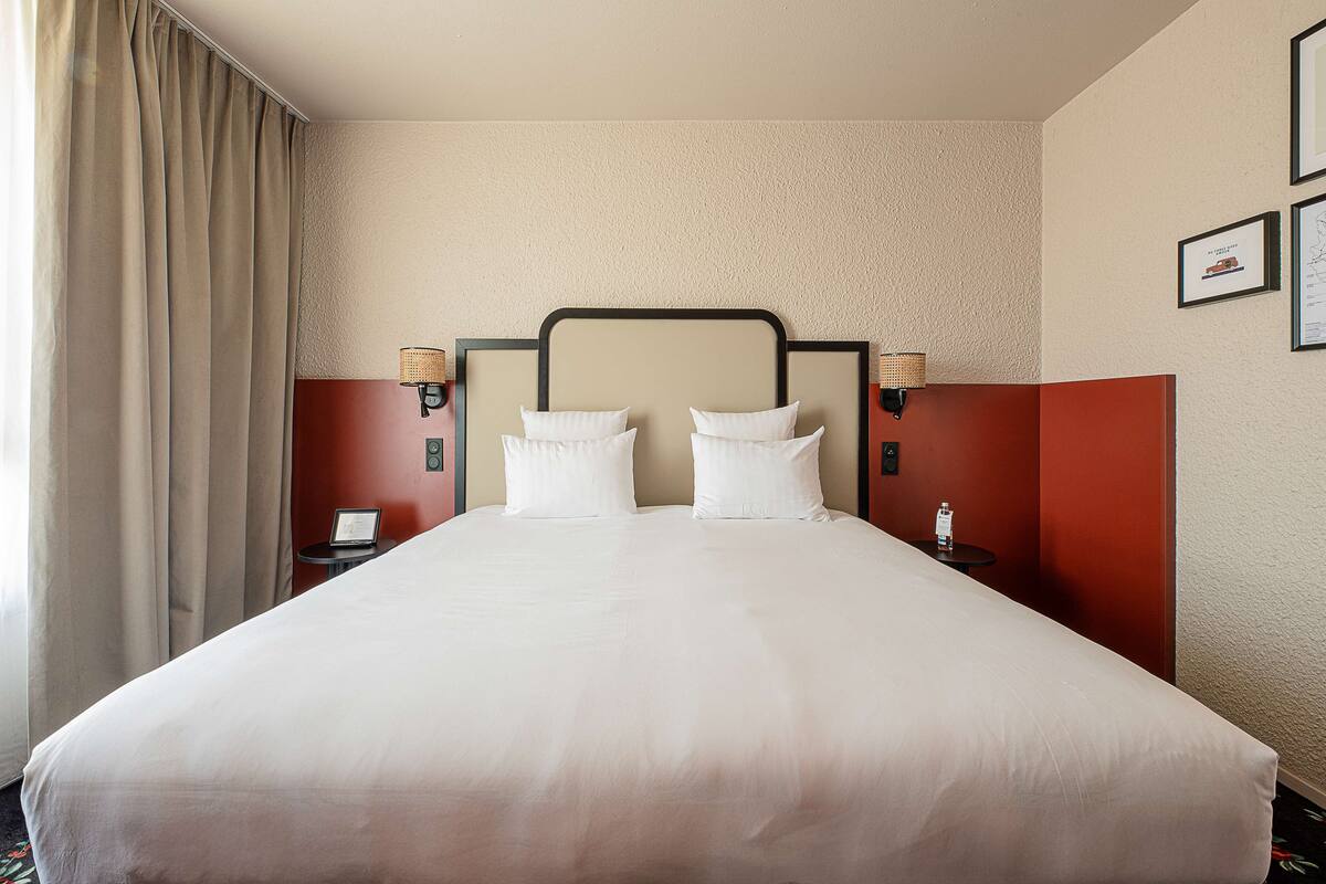 A hotel room with a large bed, two bedside tables, a headboard, and a wall-mounted lamp.