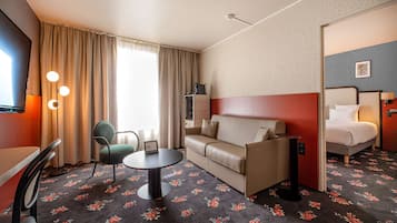 A hotel room with a sofa, a small table, a chair, a bed, and a TV.