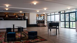 Eine großzügige Lobby mit Barbereich, einer Treppe zu einer weiteren Ebene und großen Fenstern, die viel Tageslicht hereinlassen.