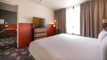 Een hotelkamer met een groot bed, een televisie, een bureau met stoel en een raam met gordijnen.