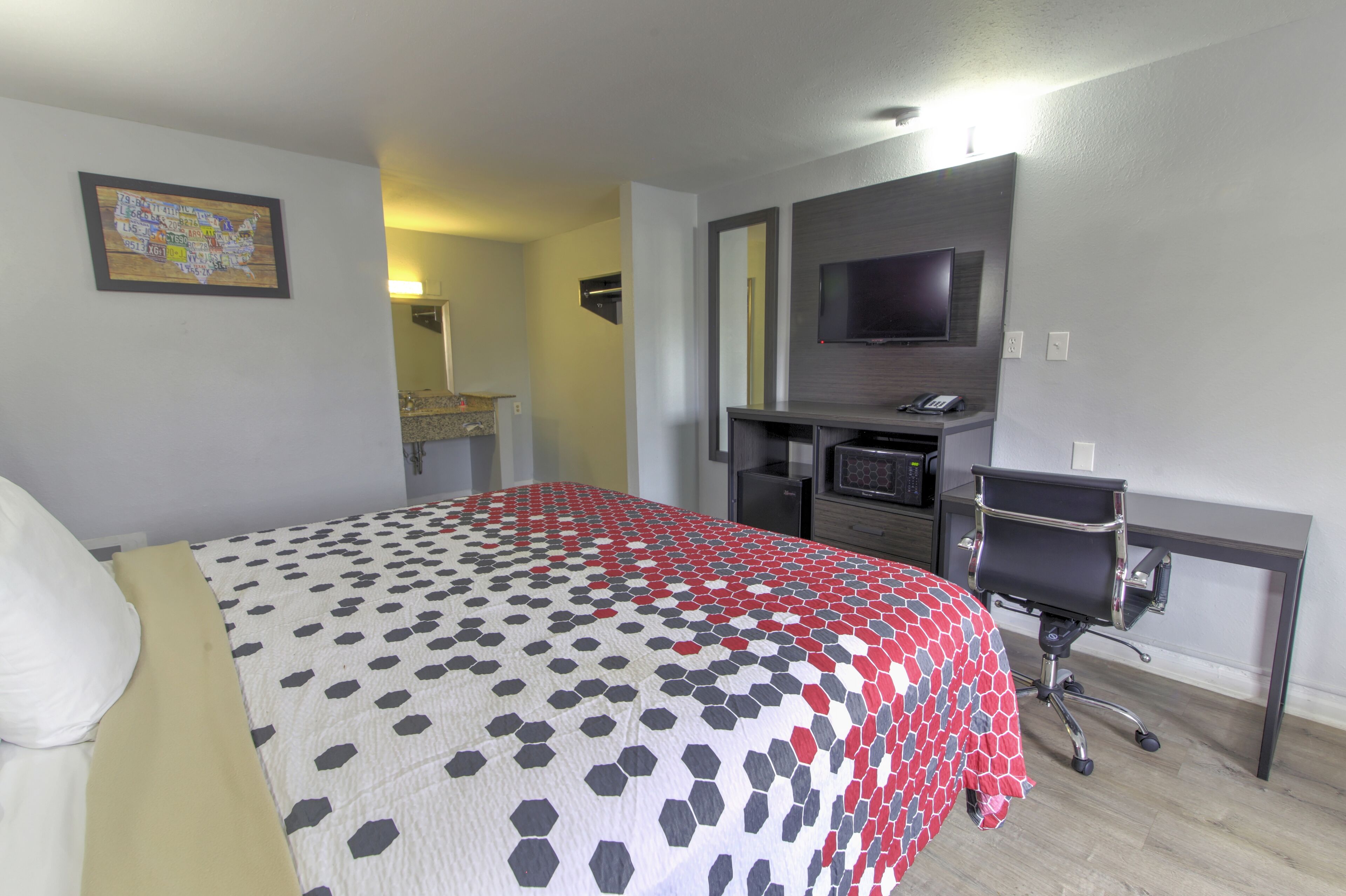 A hotel room with a bed, a desk, a chair, a TV, and a bathroom.