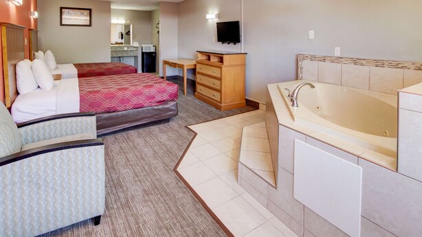 Quarto de hotel com duas camas, uma escrivaninha, televisão, banheiro com banheira e uma pequena cozinha.