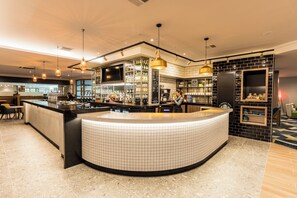 A modern bar area with a curved counter, overhead lighting, and a large television screen. - Holiday Inn Bristol-Filton by IHG (Bristol)