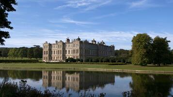 A large, historic building with a symmetrical facade, a reflection in the water, and a well-maintained lawn.