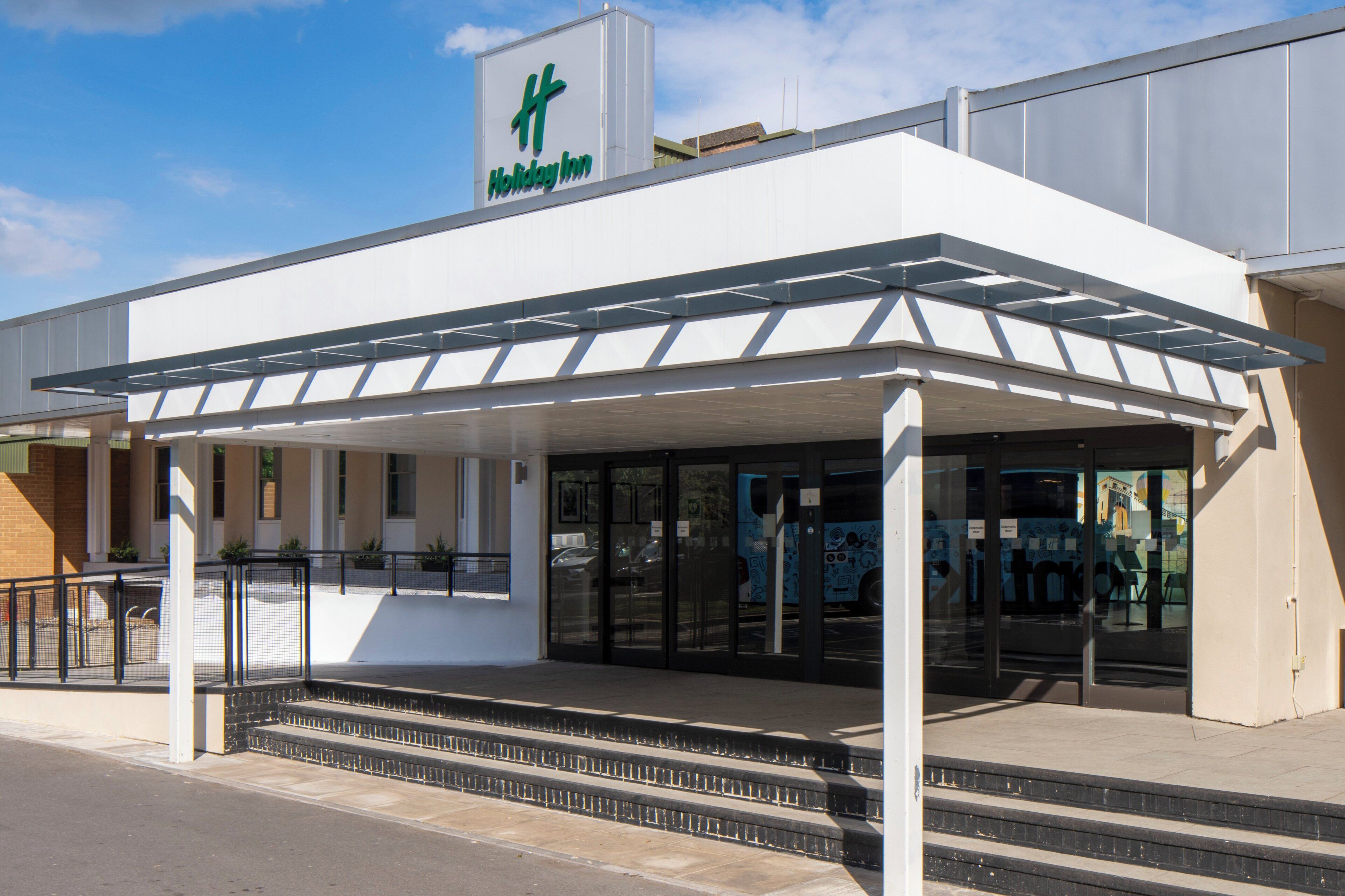 Entrada de un hotel Holiday Inn con un vestíbulo cubierto y escaleras que conducen a la entrada.