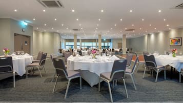 A large conference room with multiple tables and chairs, equipped with ceiling lights and air conditioning units.