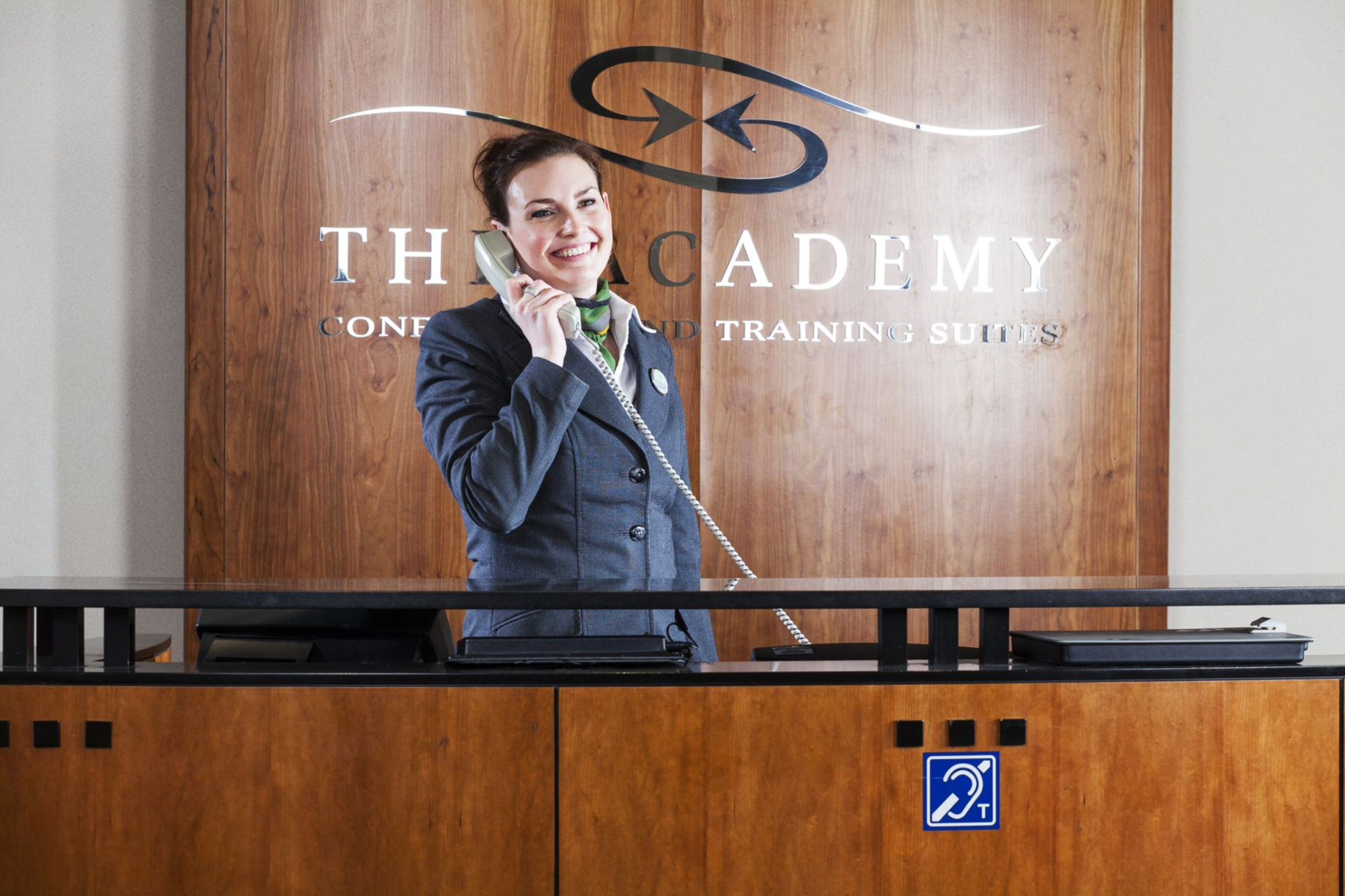 Una mesa de recepción con un fondo de madera que muestra los textos 'THC ACADEMY' y 'TRAINING SUITES'.