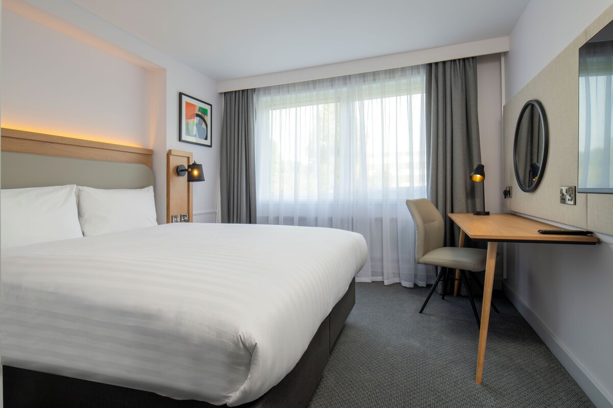 Een hotelkamer met een groot bed, een bureau, een stoel en een raam met gordijnen.
