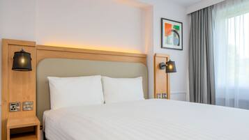 A hotel room with a large bed, wooden headboard, bedside lamps, a nightstand, and a framed picture on the wall.