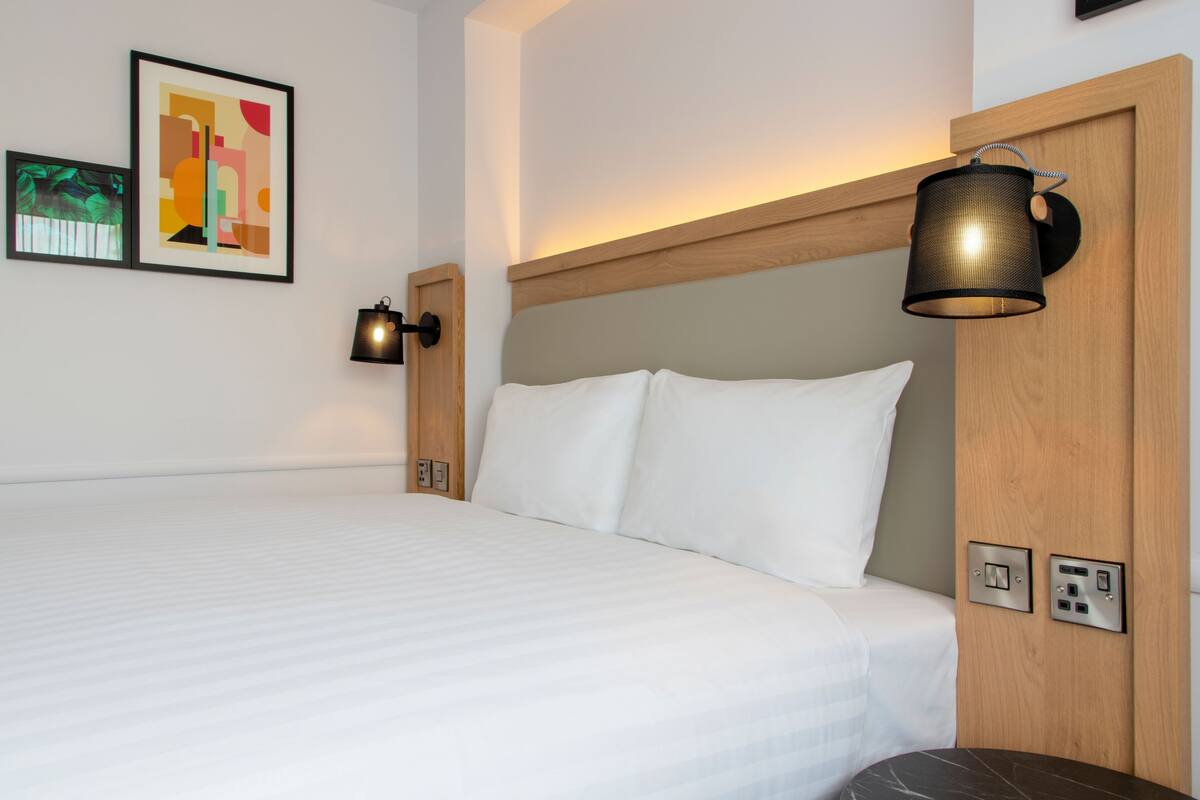 A hotel room with a large bed, a wall-mounted lamp, and a framed picture.