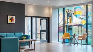 A modern hotel lobby with a teal sofa, wooden coffee table, and yellow chairs around a small table. - Holiday Inn Bristol-Filton by IHG (Bristol)