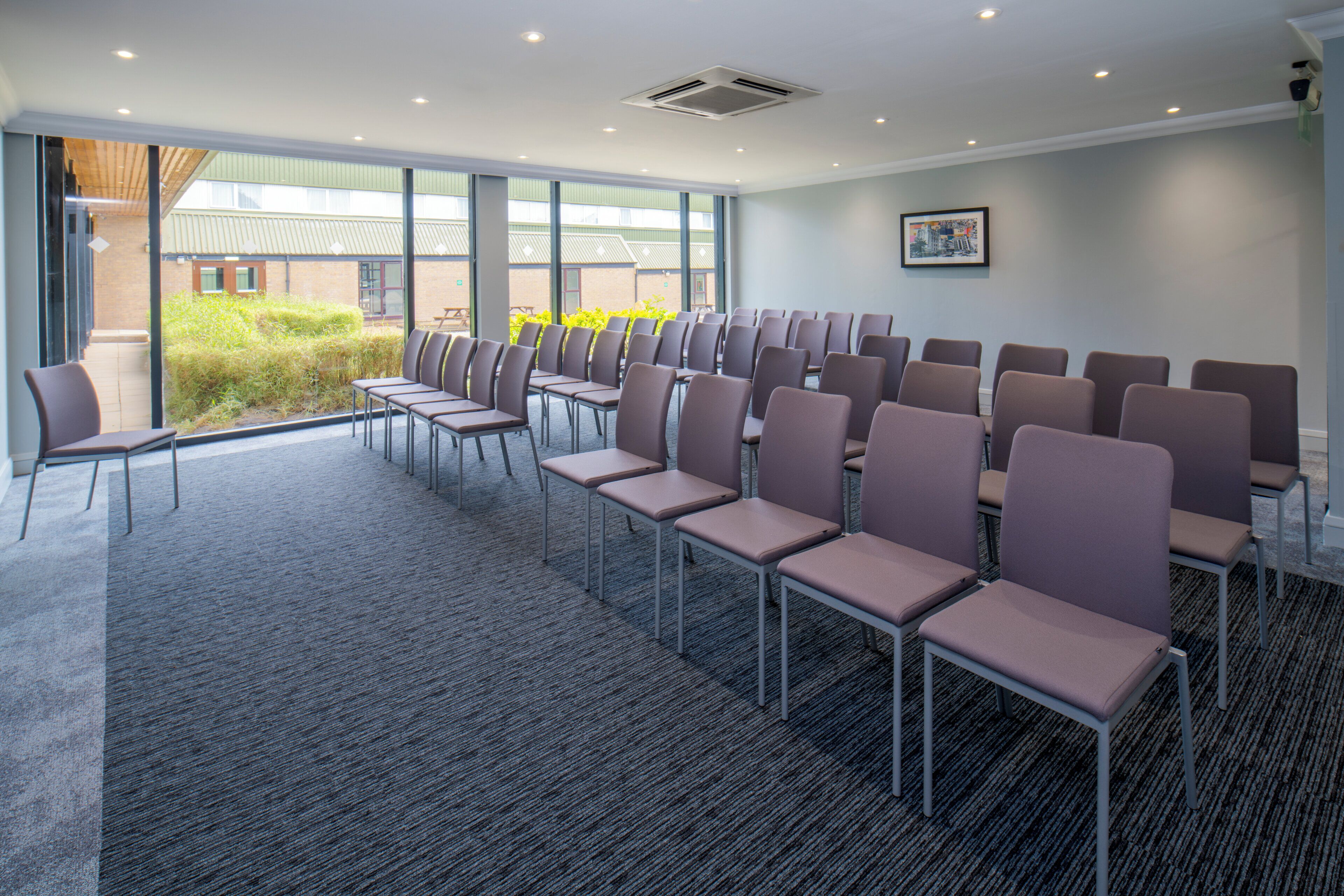 Une salle de conférence avec des rangées de chaises, de grandes fenêtres et un sol recouvert de moquette.