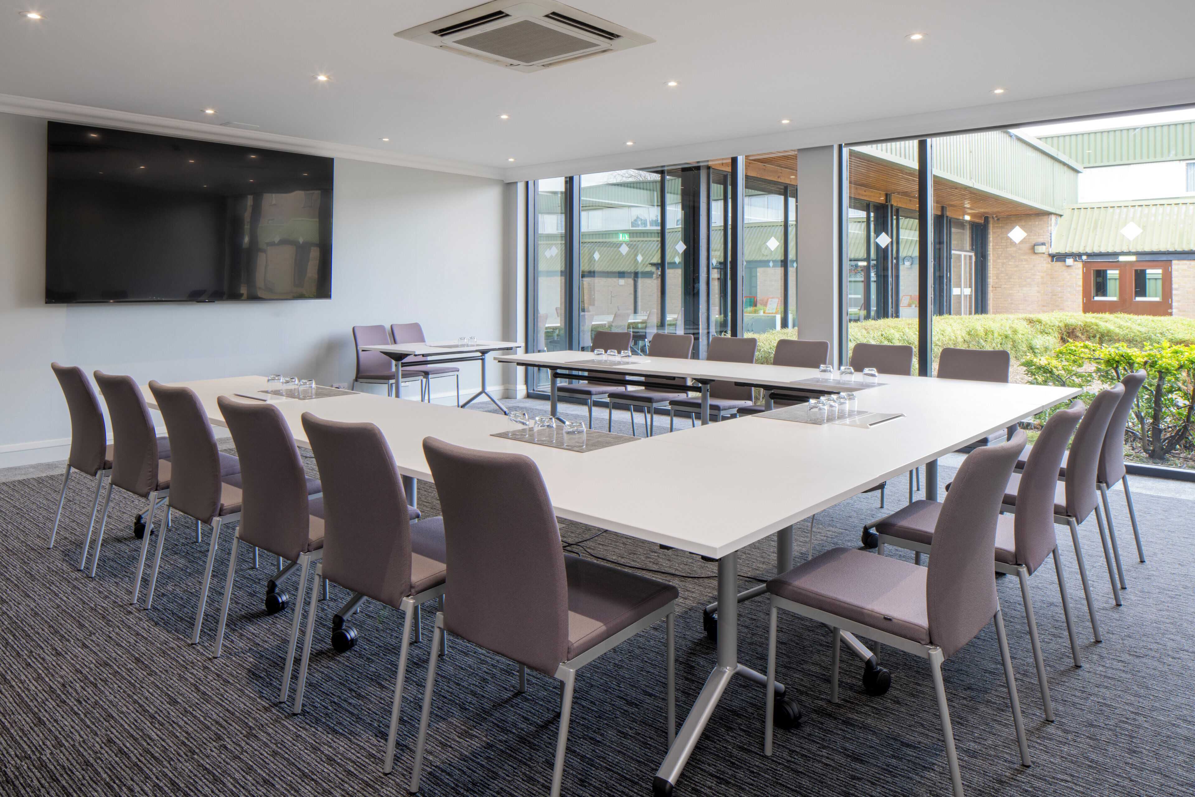 A conference room with a large table, chairs, a flat-screen TV, and large windows.