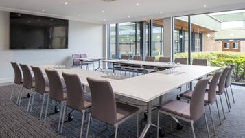 A conference room with a large table, chairs, a flat-screen TV, and large windows.