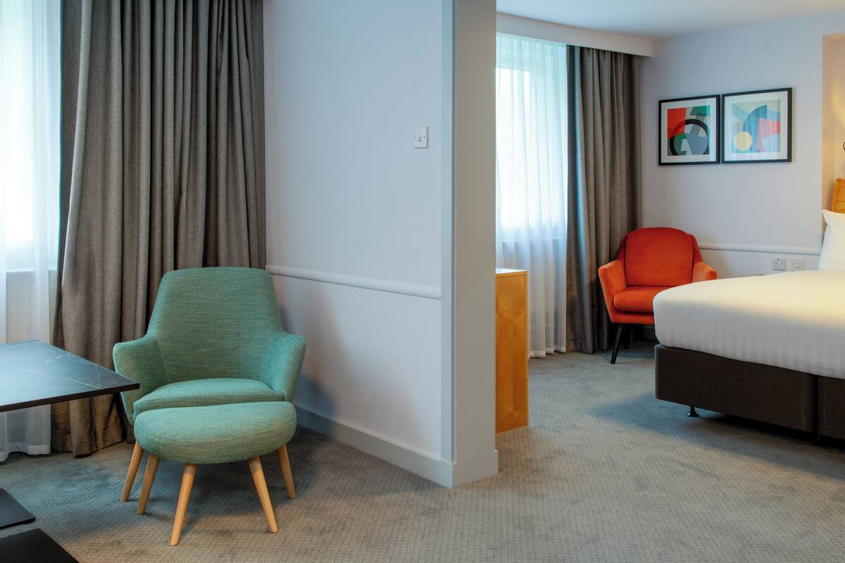 A hotel room with a bed, two chairs, a desk, and a window with curtains.