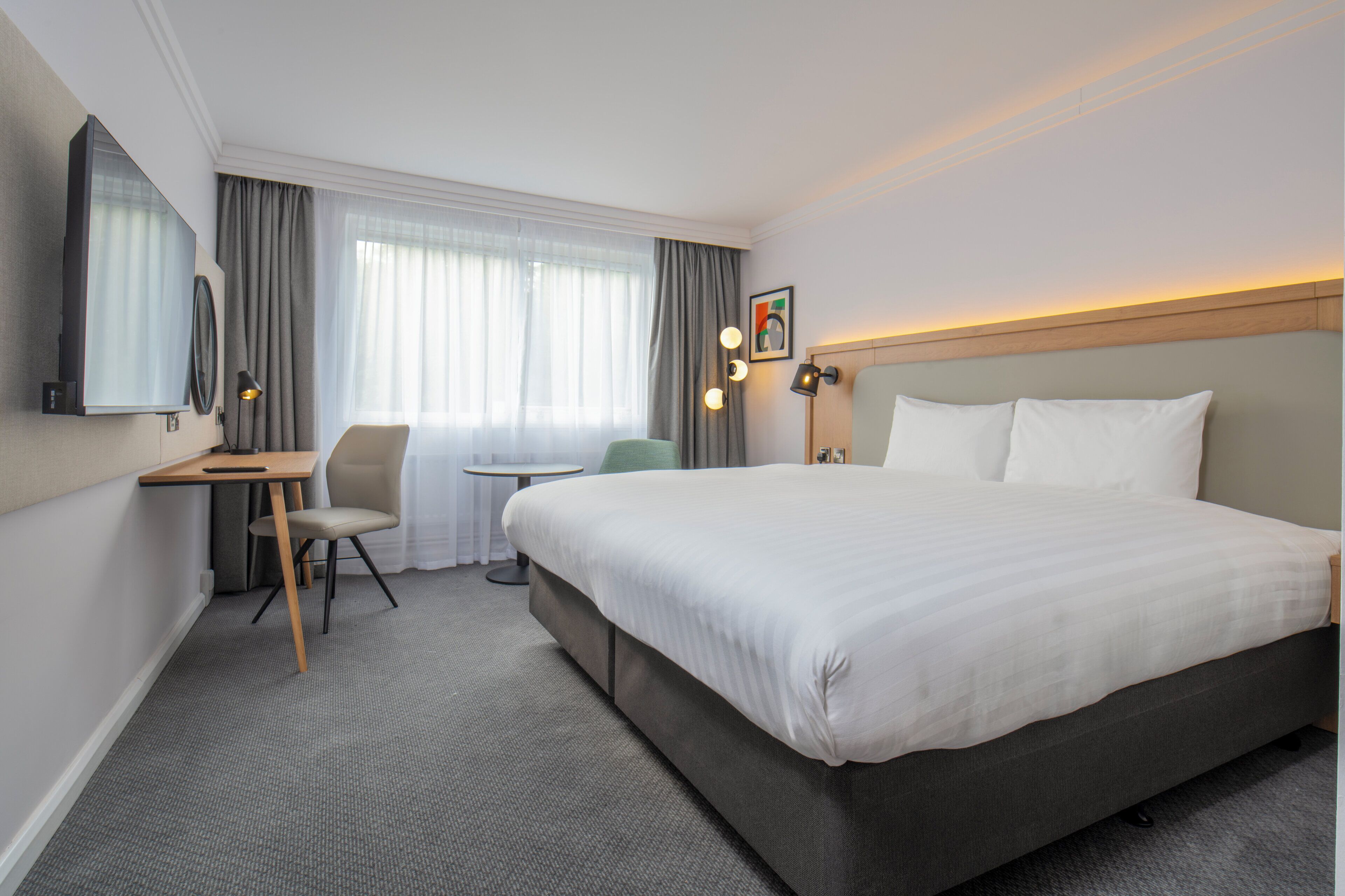 Una camera d'albergo con un letto grande, una scrivania, una sedia, un tavolino e un televisore.