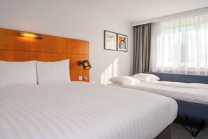Relax in this stylish room with a large bed and a smaller bed, featuring a wall-mounted light fixture and a picture frame.