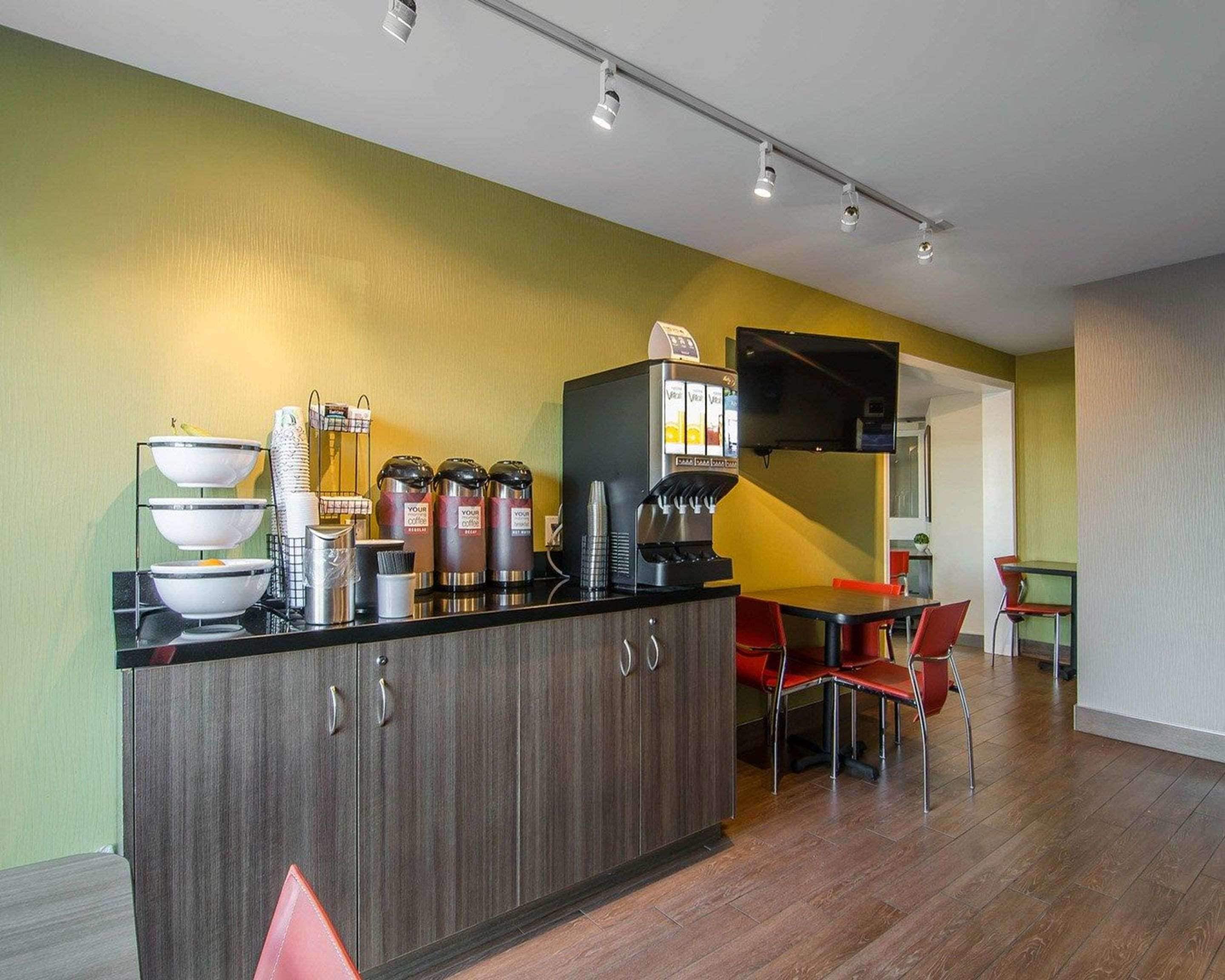 A modern kitchen area with a coffee station, including a coffee machine and dispensers, and a dining area with red chairs and a table.