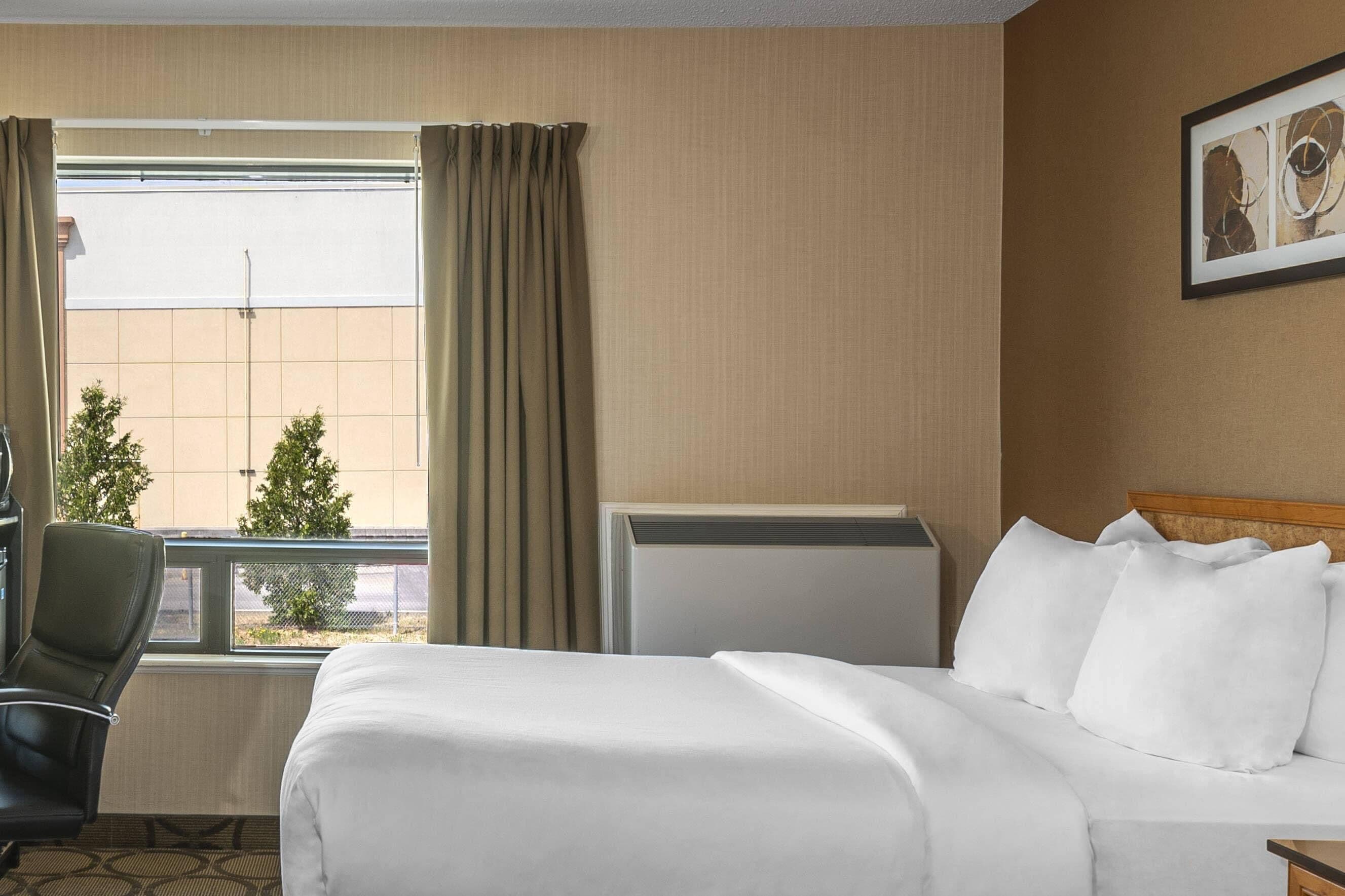 A hotel room with a bed, a chair, a radiator, and a window with curtains.