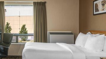 A hotel room with a bed, a chair, a radiator, and a window with curtains.