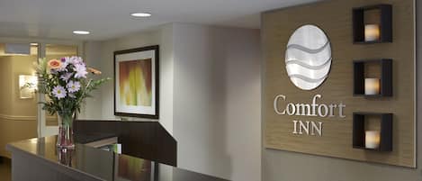 A reception area with a dark reception desk, a vase of flowers, and a sign that reads "Comfort Inn."