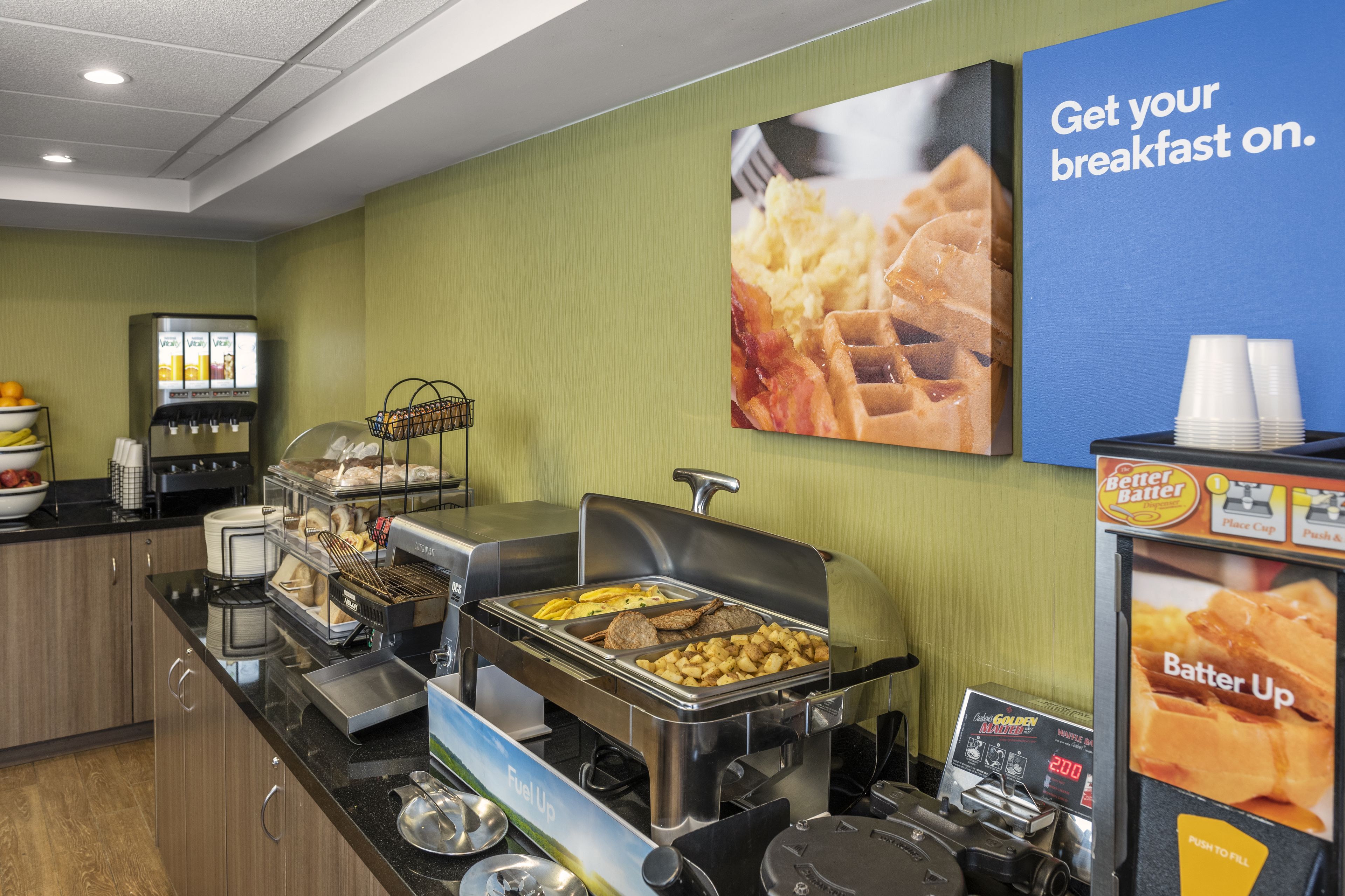 A breakfast buffet with various food options, a coffee machine, and a sign encouraging guests to get their breakfast on.