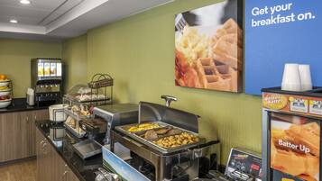 A breakfast buffet with various food options, a coffee machine, and a sign encouraging guests to get their breakfast on.