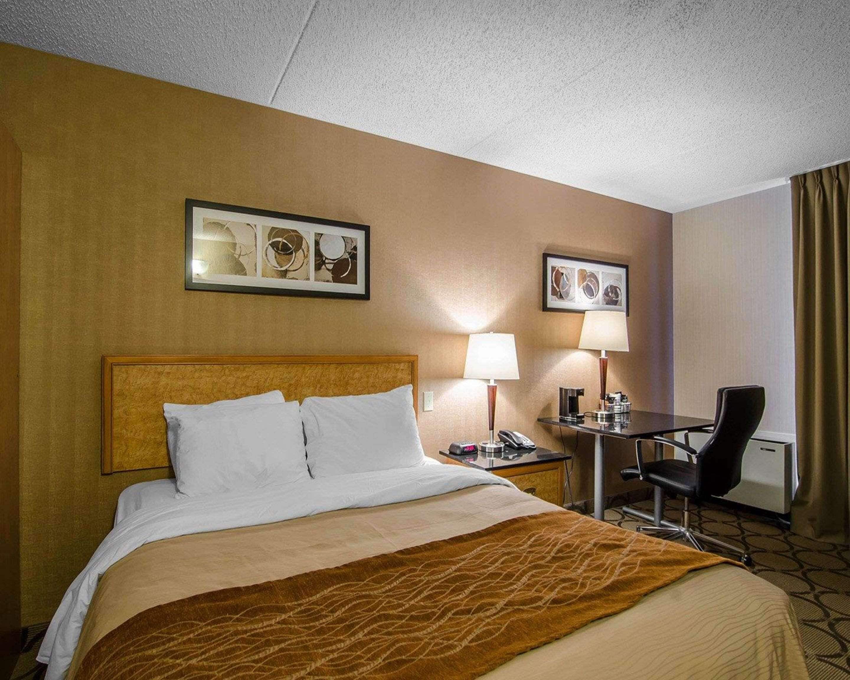 A hotel room with a large bed, two bedside tables with lamps, a desk with a chair, and artwork on the walls.
