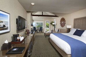 A hotel room with a large bed, a desk with a computer, a TV, and a view of the outdoors.