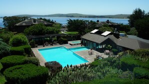 A large swimming pool surrounded by lush greenery, with a view of a body of water and hills in the background. - The Inn at the Tides (Bodega Bay)