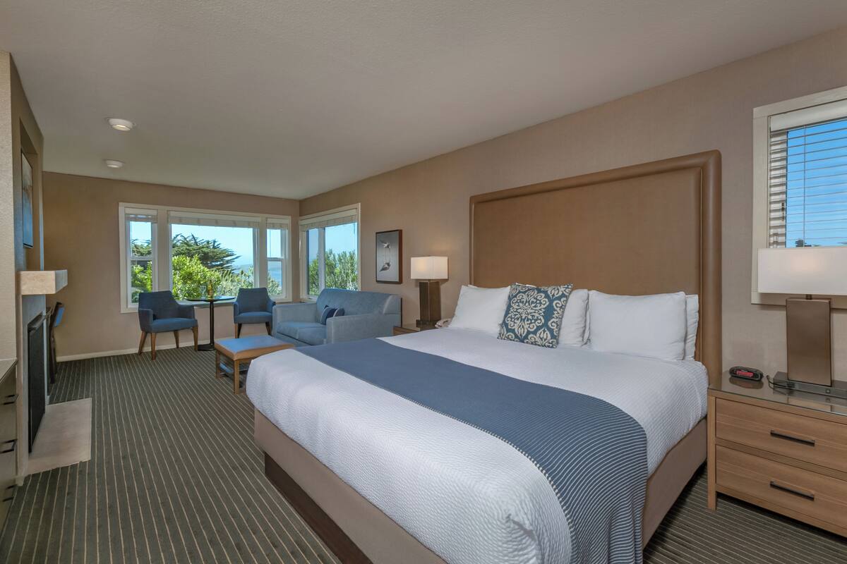 A hotel room with a large bed, two armchairs, a small table, and a desk with a chair.