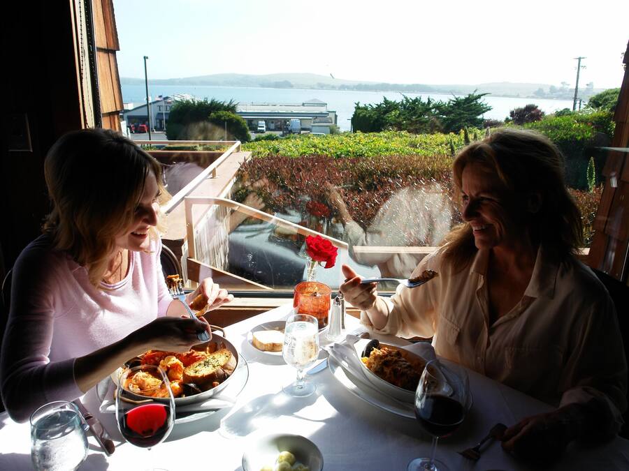 Duas pessoas jantando à mesa com vista para o mar e as colinas.