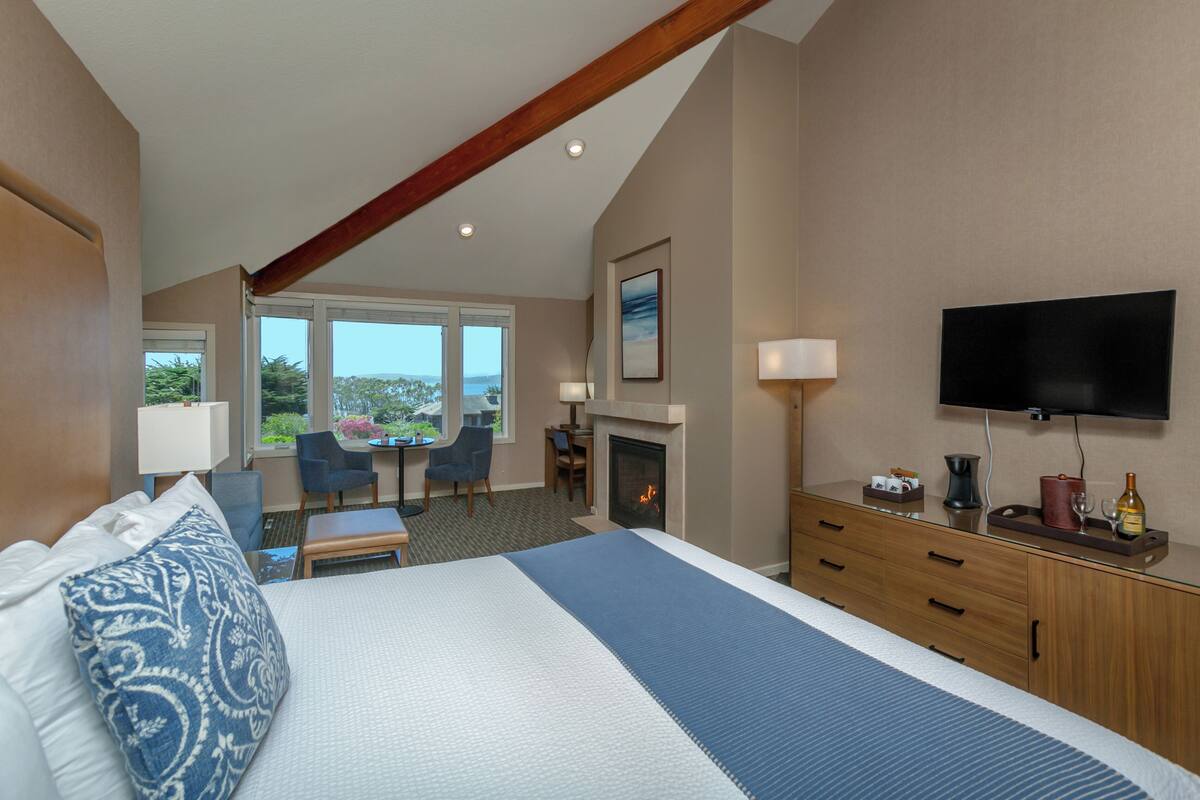 A hotel room with a large bed, a desk, a chair, a fireplace, and a TV.