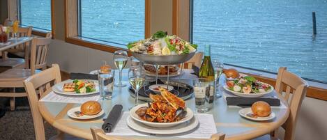 Une table à manger dressée avec des plats de fruits de mer, des verres à vin et une vue sur l’eau.