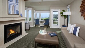 A hotel room with a fireplace, a sofa, a coffee table, and a view of the outdoors. - The Inn at the Tides (Bodega Bay)