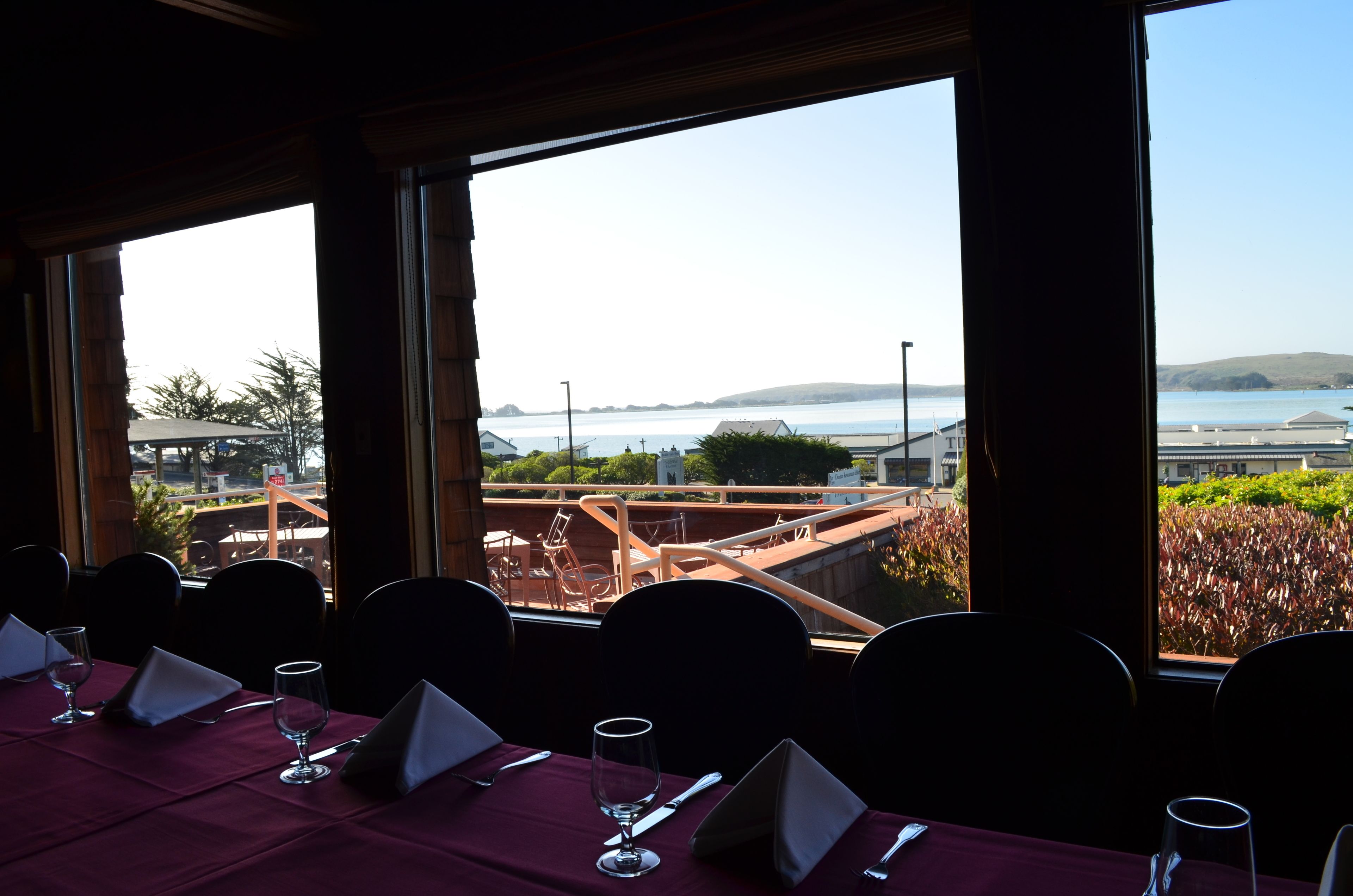Un espace repas avec des tables dressées pour le service, de grandes fenêtres offrant une vue sur le bord de l’eau et sur des collines lointaines.