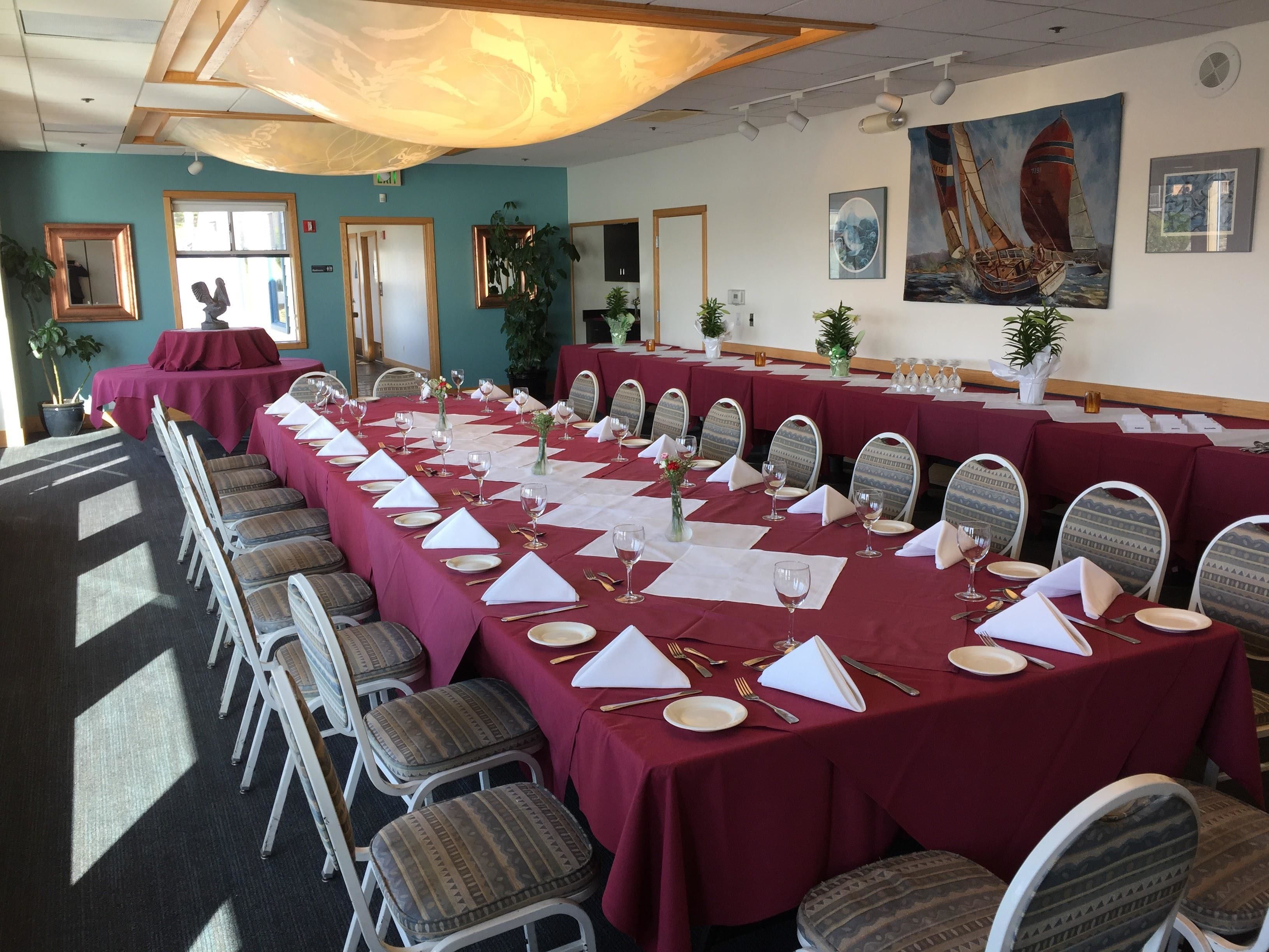 A conference room with long tables set for a formal event, equipped with chairs, tables, and various table settings.