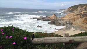 A coastal landscape with rocky cliffs, a sandy beach, and a person walking along the shore. - The Inn at the Tides (Bodega Bay)